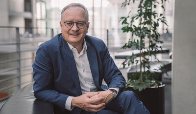 Der Parteivorsitzende der SPD Baden-Württemberg Andreas Stoch sitzt auf einer Couch in einer Lobby und lächelt in die Kamera.
